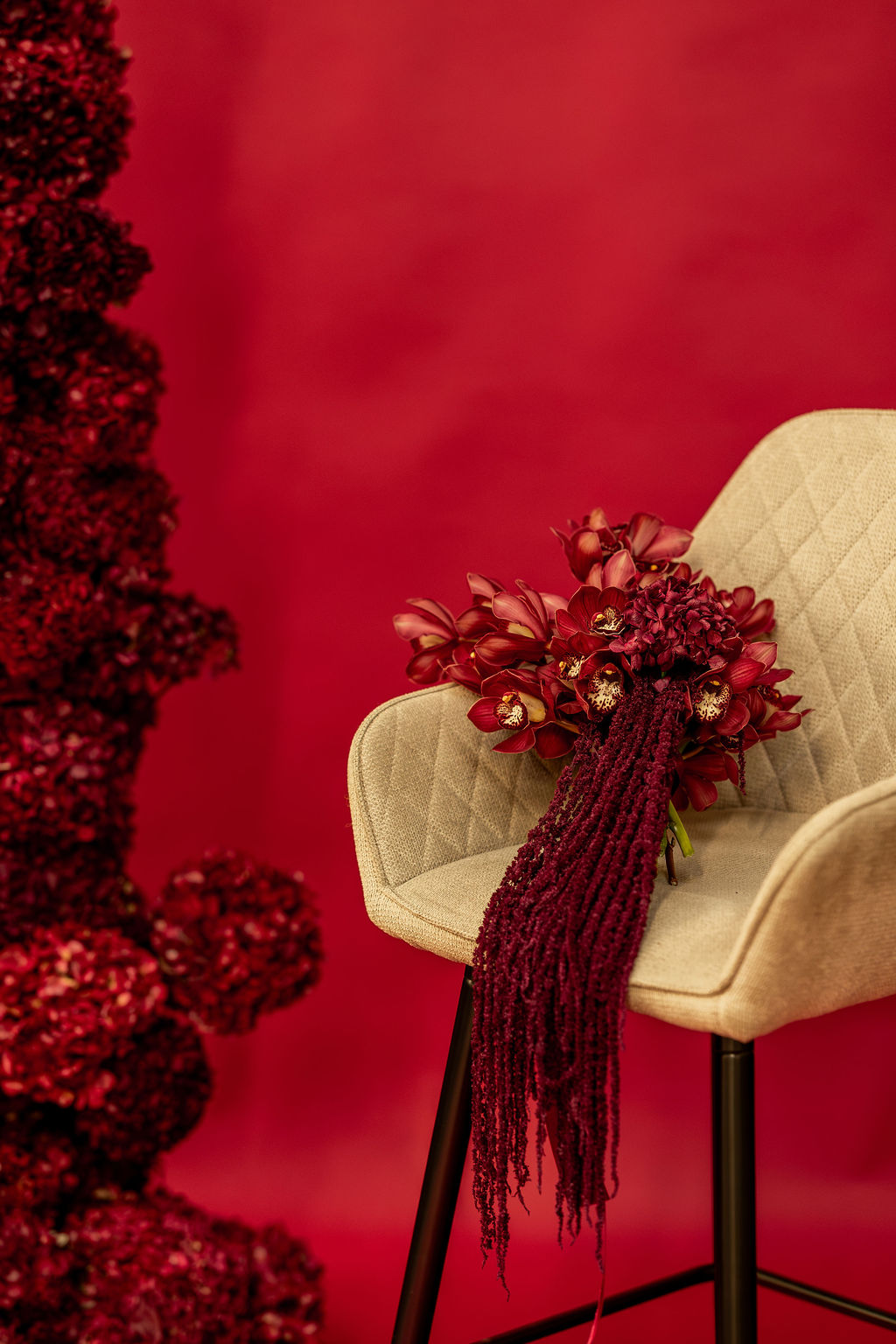 Hand-dried, hand-painted deep red bouquet by Alanah Conner Wedding Florals resting on a chair beside a floral arch
