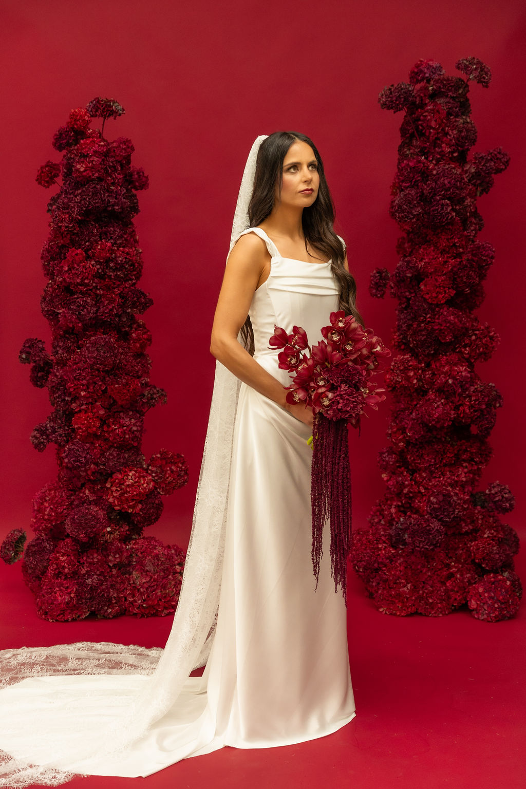 Bride in a satin square-neck gown and chantilly lace veil holding deep red orchids, photographed for FOUNDATION by Sarah Stoute
